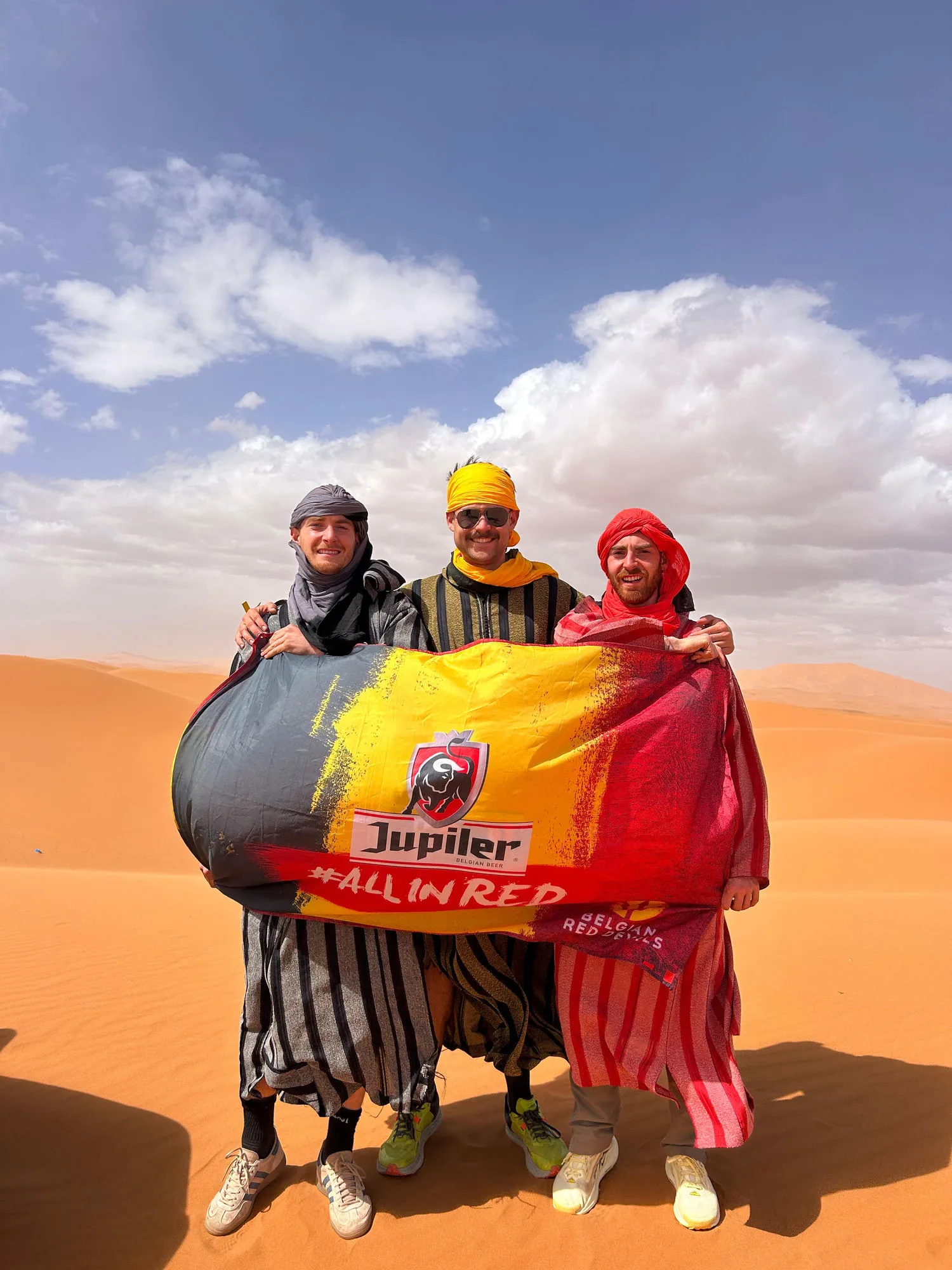 Het team in djellaba's met Belgische vlag op de Sahara-duinen bij MDS Marokko